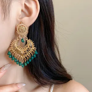 Detailed view of ethnic style gold filigree earrings with green beads on model.