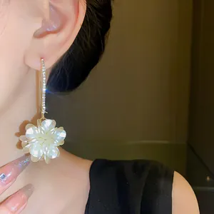 Macro detail of white flower drop earrings with sparkling rhinestones worn on ear