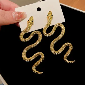 Vue détaillée des boucles d'oreilles serpent dorées avec yeux en gemme verte et écailles