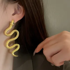Vue détaillée de boucles d'oreilles serpent dorées avec des yeux brillants en strass.