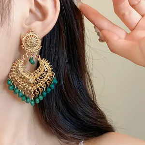 Detailed macro view of ornate gold ethnic drop earrings with green beads worn by model