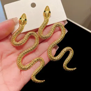 Détail de boucles d'oreilles serpent dorées avec des yeux en pierres précieuses vertes