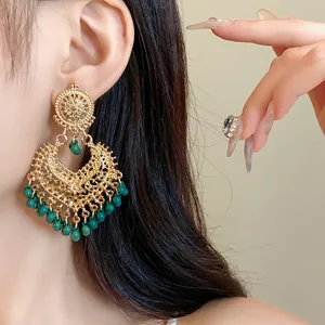 Macro view of ornate ethnic gold hollow dangling earrings decorated with green beads