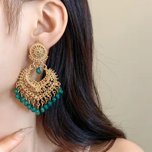 Detail close-up of ornate gold ethnic style chandelier earrings with green beads on model