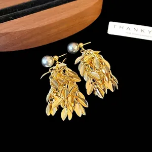 Elegant leaf tassel gold drop earrings featuring grey faux pearls on a black background