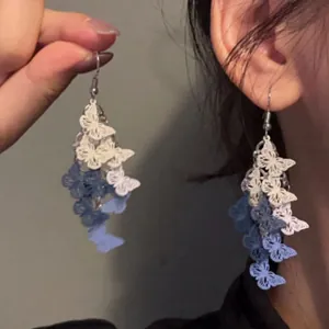 Primo piano dettagliato di eleganti orecchini a nappa con farfalle blu e bianche sull'orecchio.