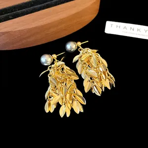 Macro detail of gold leaf tassel earrings with elegant grey pearls on black background