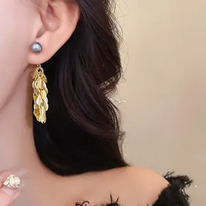 Close-up detail of elegant leaf tassel earrings with grey pearl stud on model's ear.