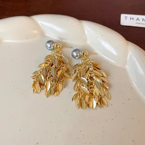 Detail view of elegant gold leaf tassel earrings with a stylish grey faux pearl accent.