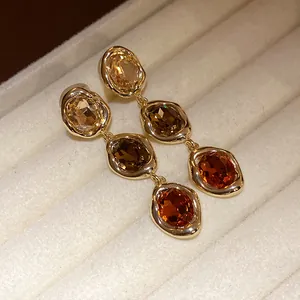 Close-up of 18k gold-plated oval dangle earrings with amber gemstones in jewelry box.