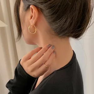 Detailed wearing shot of elegant twisted gold hoop earrings and minimalist ring