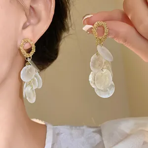 Primer plano de elegantes pendientes dorados con detalles de flecos de concha blanca