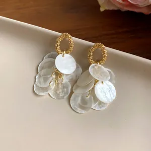 Primer plano de pendientes de borla de concha estilo francés con elegantes pernos de oro.