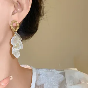Primer plano de elegantes pendientes dorados con pétalos de concha blanca en cascada
