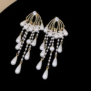 Detalle de pendientes de borla dorados con circonita y elegantes perlas de gota.