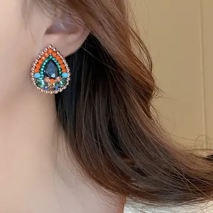 Detail shot of a vintage teardrop earring with vibrant multi-color stones on a model.