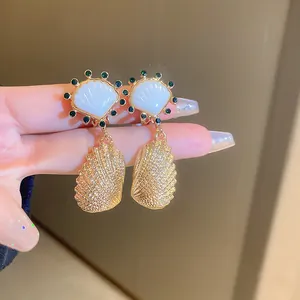Detailed macro shot of vintage gold shell earrings with green rhinestones and white inlay