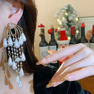 Primer plano detallado de pendientes largos dorados con perlas de gota y circón.