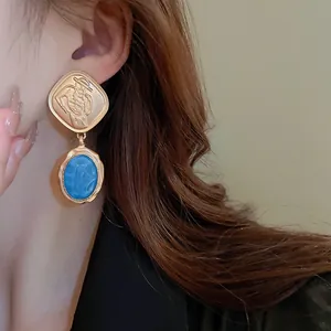 Close-up of vintage French style drop earrings with blue oval stone and gold relief.