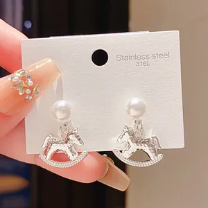 Detail shot of pearl rocking horse earrings with 316L stainless steel display card.