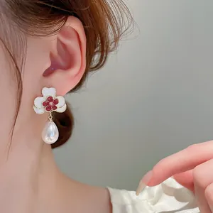 Close-up of French vintage white flower earrings with red centers and waterdrop pearl drops