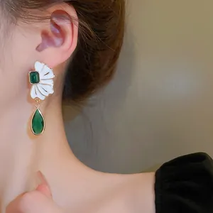 Close-up of French vintage floral earrings with green teardrop gemstones on model