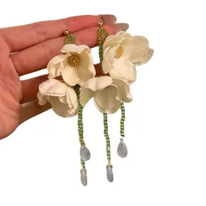 Mano che tiene eleganti orecchini a fiore in tessuto bianco con nappe di perline verdi