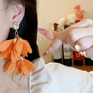 Primo piano di eleganti orecchini a fiori in chiffon arancione con dettaglio in cristallo.