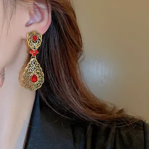 Close-up view of vintage palace style drop earrings with red teardrop stones on a model