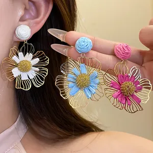 Close-up of handmade raffia flower drop earrings in white, blue, and pink colors