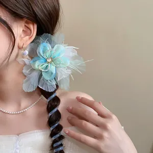 Detail of a blue fabric flower hair tie with a spiral telephone wire design on a braid.