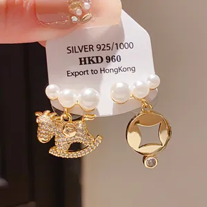 Detail of asymmetric pearl earrings with crystal-studded horse and geometric charms