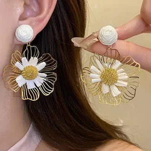 Close-up of elegant white raffia flower drop earrings with silver needles on ear.