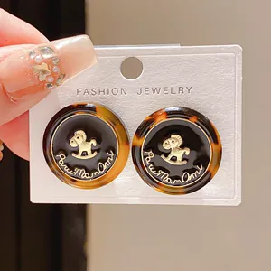 Close-up of vintage tortoiseshell stud earrings with golden rocking horse motif