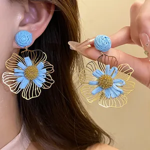 Detailed close-up of blue raffia flower pendant earrings featuring gold hollow petals