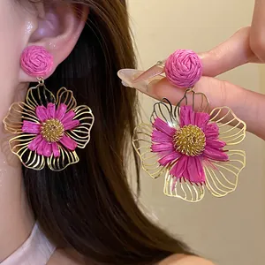 Close-up of pink raffia flower earrings with intricate gold wire centers