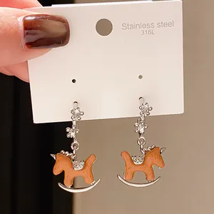 Detailed close-up of orange enamel rocking horse earrings on 316L stainless steel display card