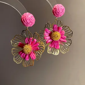 Macro view showing the intricate pink raffia and golden wire petals of flower earrings.