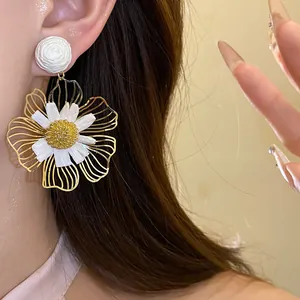 Close-up detail of large gold wire and white raffia flower drop earrings worn on the ear