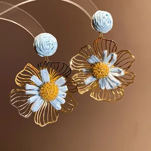 Close-up of blue raffia flower earrings with delicate gold metal frames for vacation.