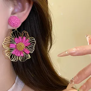 Detailed view of vacation style pink raffia flower drop earrings worn on model's ear