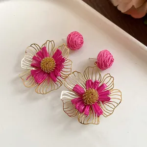 Close-up detail of handmade pink raffia flower earrings with elegant gold hollow-out petals