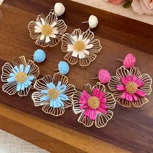 Detail view of raffia floral drop earrings in white, blue and pink on wooden board