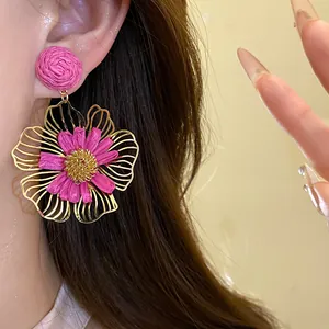 Close-up of pink Raffia grass flower earring with golden hollow petals on ear