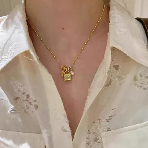 Primo piano di collana regolabile dorata con lucchetto in zirconi e croce indossata da modella.