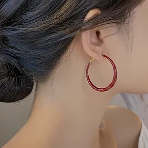 Dettaglio laterale di una modella che indossa grandi orecchini a cerchio in smalto rosso.