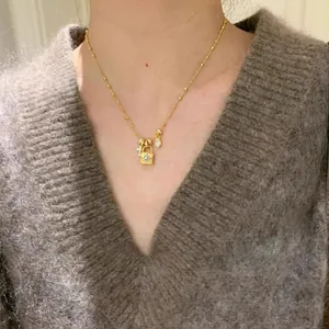 Dettaglio di una collana dorata con pendente a lucchetto e croce con zirconi su modella