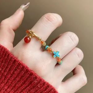 Primo piano di anello elastico con perline dorate, occhio di tigre e charm fiore blu.