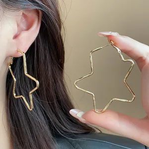 Detalle de pendientes de aro dorados grandes con forma de estrella lucidos por una modelo