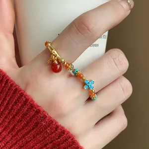 Dettaglio di un anello elastico placcato oro con perline colorate e quadrifoglio